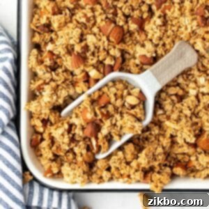 A scoop taking a portion of golden-brown granola from a baking pan.