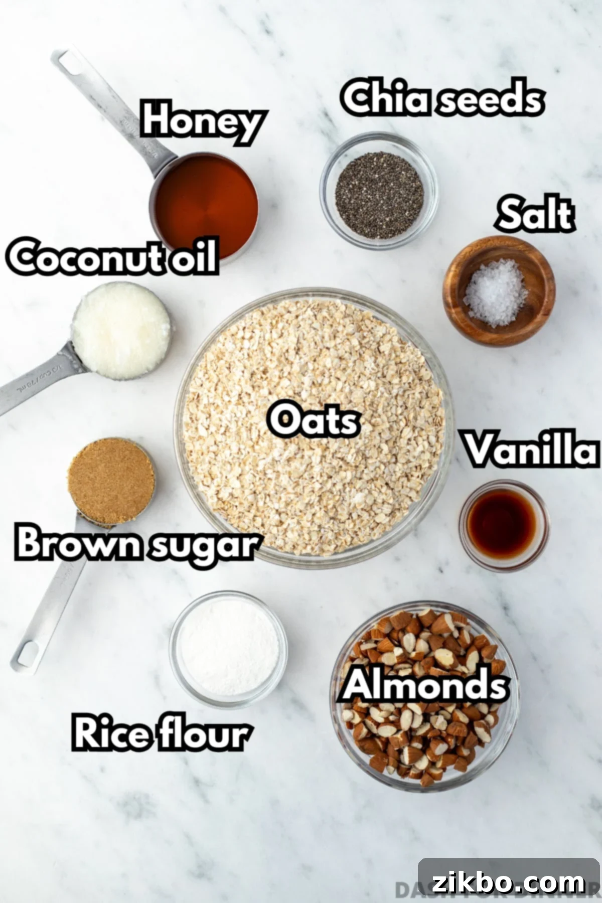 A bowl of quick oats, surrounded by the essential ingredients needed to make delicious granola, including honey, brown sugar, chopped almonds, vanilla extract, and chia seeds.