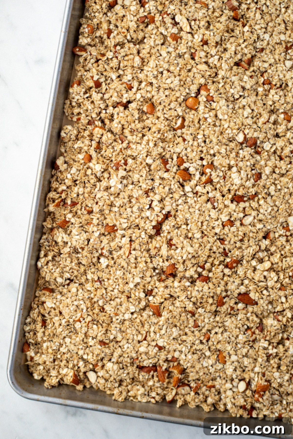 A sheet pan filled with the granola mixture, evenly spread and dotted with chopped almonds, ready to be baked.