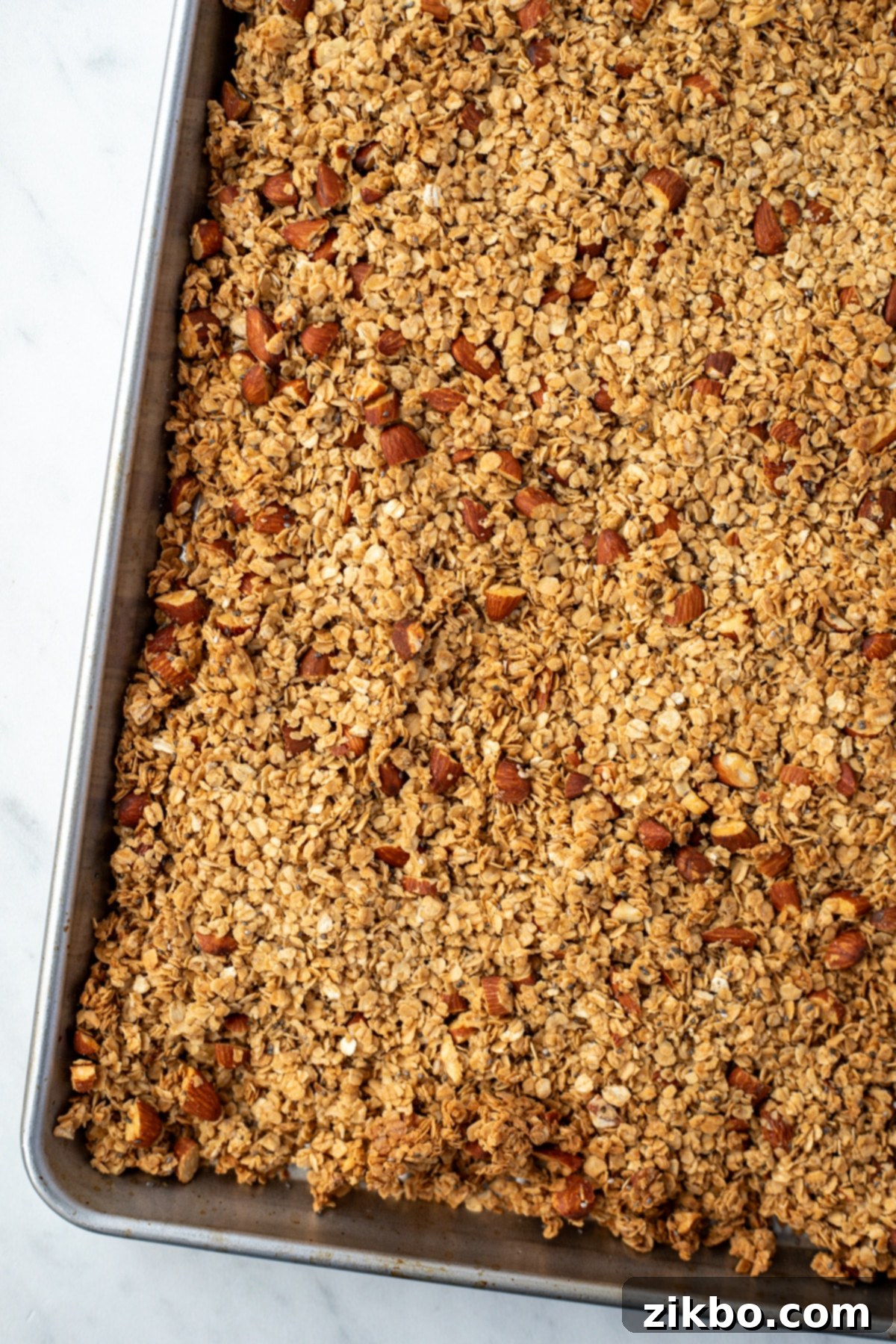 A sheet pan filled with baked granola, showing golden-brown oats, perfectly toasted almonds, and lightly browned edges.