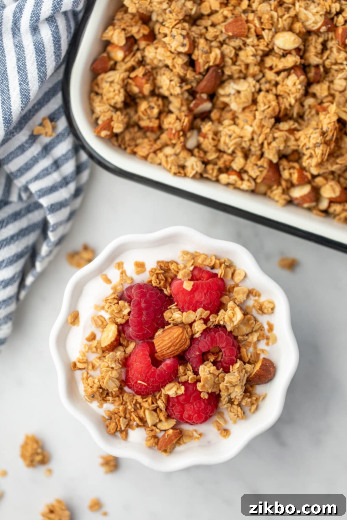A small bowl of creamy yogurt elegantly topped with fresh raspberries and a generous sprinkling of golden-brown granola.