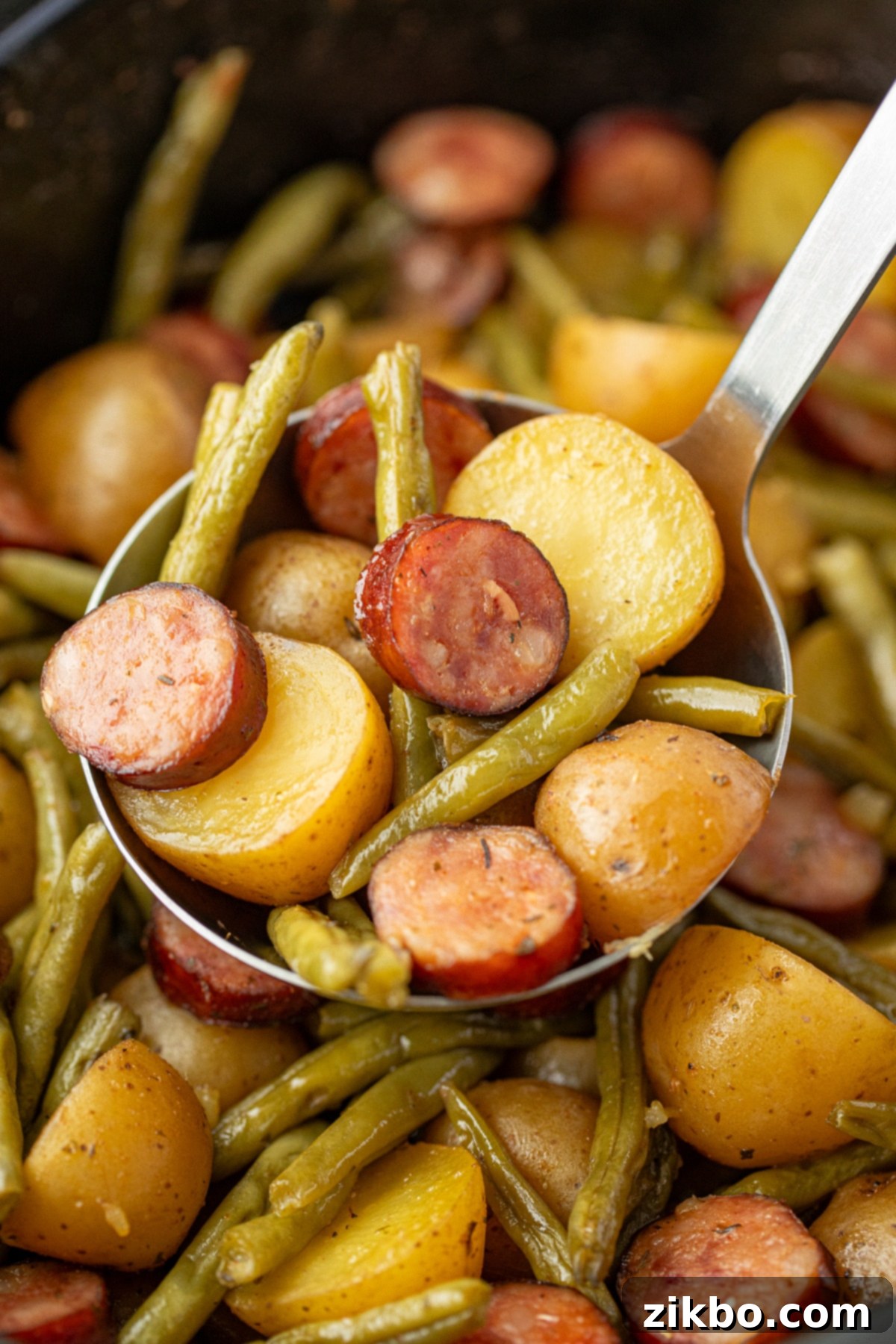 A ladle scooping tender potatoes, savory sausage, and vibrant green beans from a bubbling slow cooker.
