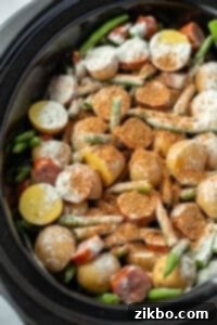 A slow cooker filled with potatoes, green beans, and sausages sprinkled with seasoning.