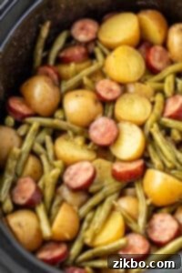 A slow cooker filled with cooked potatoes, green beans, and smoked sausage.