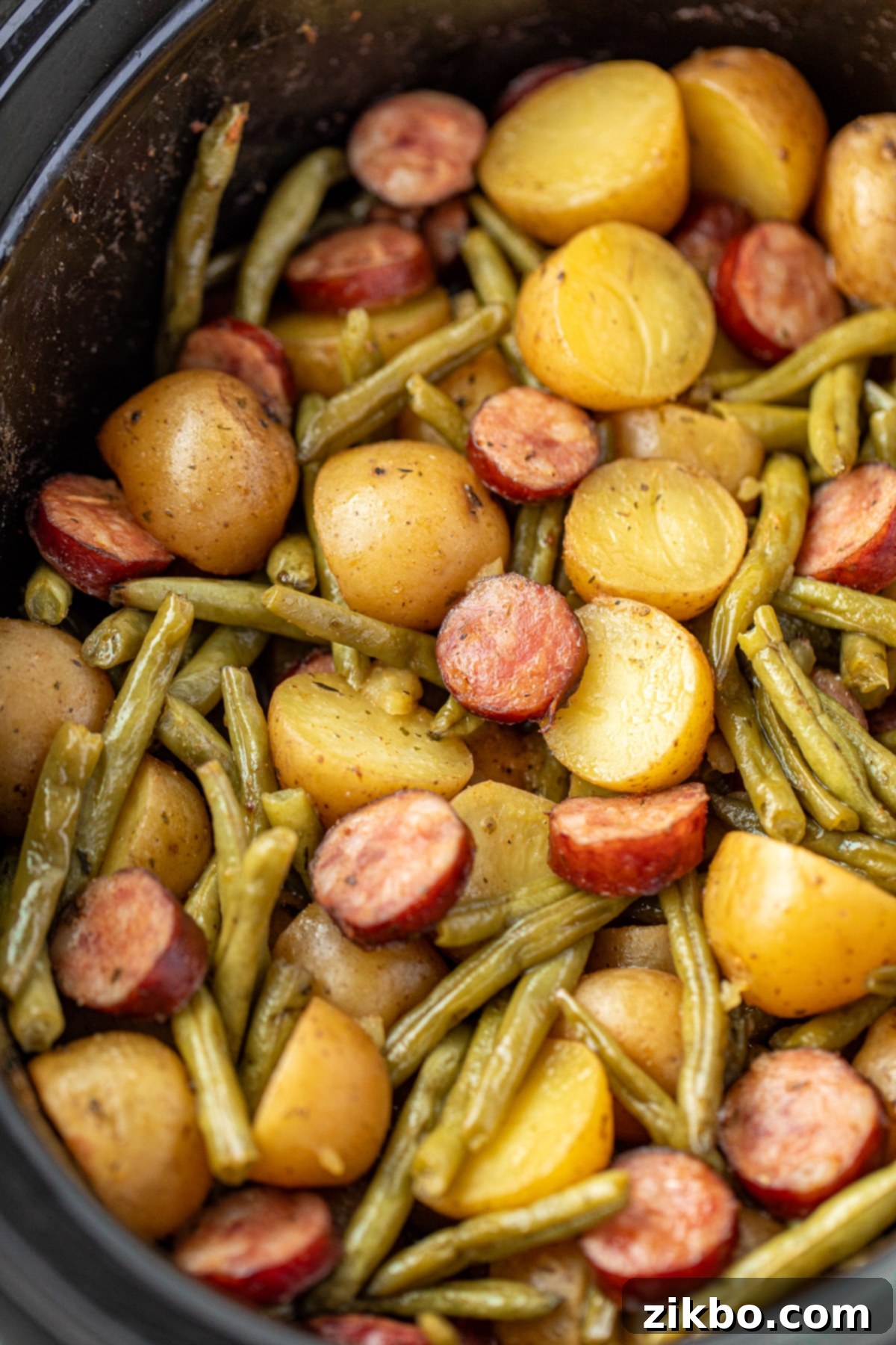 A slow cooker revealing perfectly cooked potatoes, tender green beans, and flavorful smoked sausage, ready to be served.