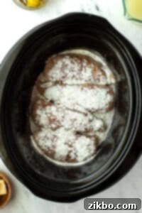 Sprinkling ranch seasoning on top of chicken breasts in a slow cooker.