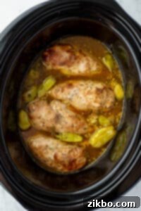 Chicken cooked in a slow cooker with seasoning, broth, and pepperoncini peppers.