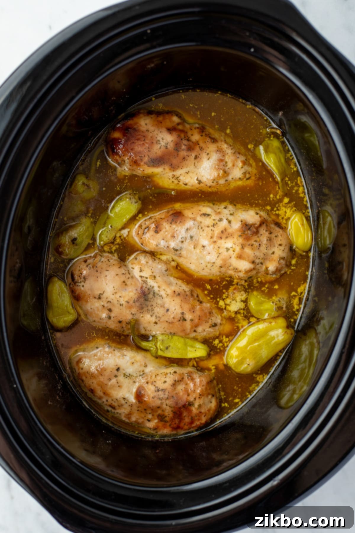 Chicken cooked in a slow cooker with seasoning, broth, and pepperoncini peppers.