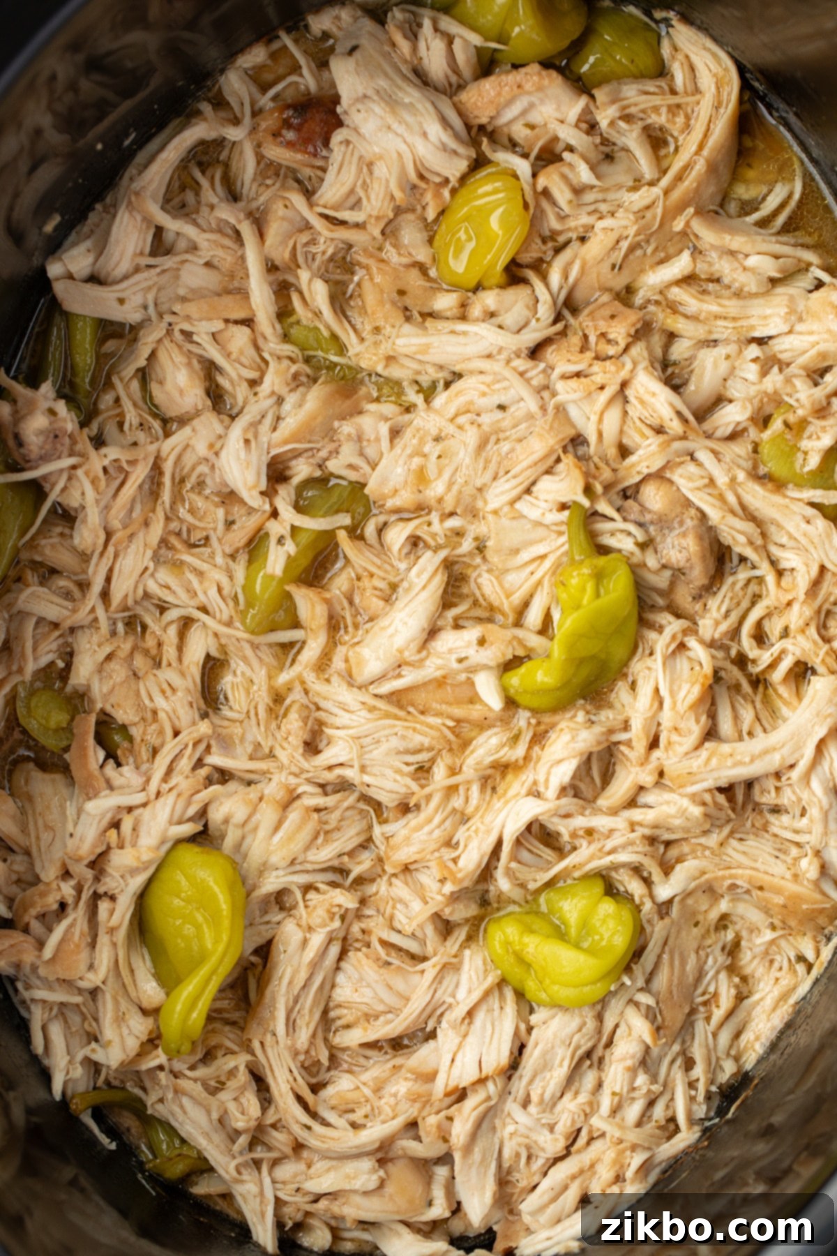 A crock pot filled with shredded chicken and topped with a few pepperoncini peppers.