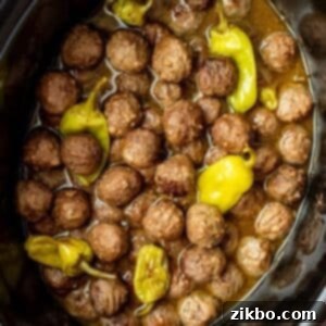 A slow cooker filled with cooked Mississippi meatballs, a thin savory sauce, and several pepperoncini peppers, ready to be served.
