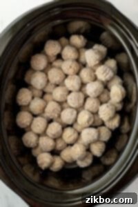 A slow cooker filled with frozen meatballs, ready for seasonings.