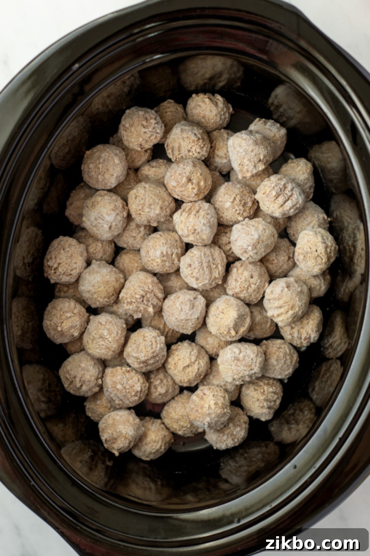 A slow cooker filled with frozen meatballs, ready for seasonings.