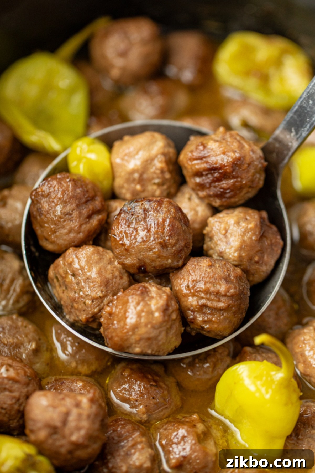 Scooping a ladle full of cooked meatballs from a large crock, highlighting the rich sauce and pepperoncini.