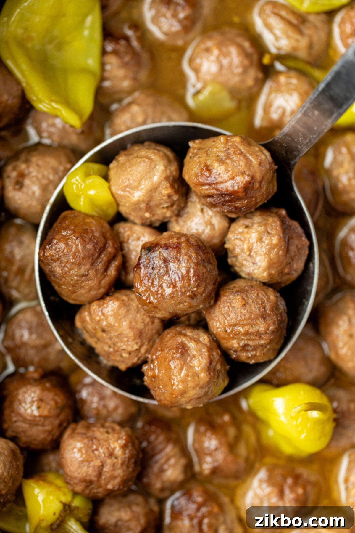 A ladle full of rich, saucy Mississippi meatballs, with several scattered pepperoncini peppers around, perfect for serving.