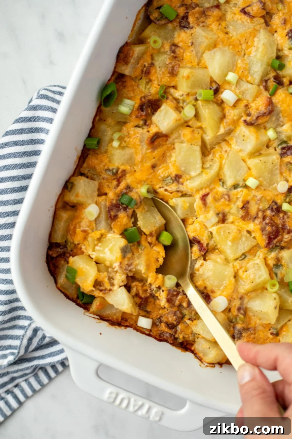 Mississippi Smothered Potatoes 7 A spoon taking a portion of potatoes from a white baking dish.