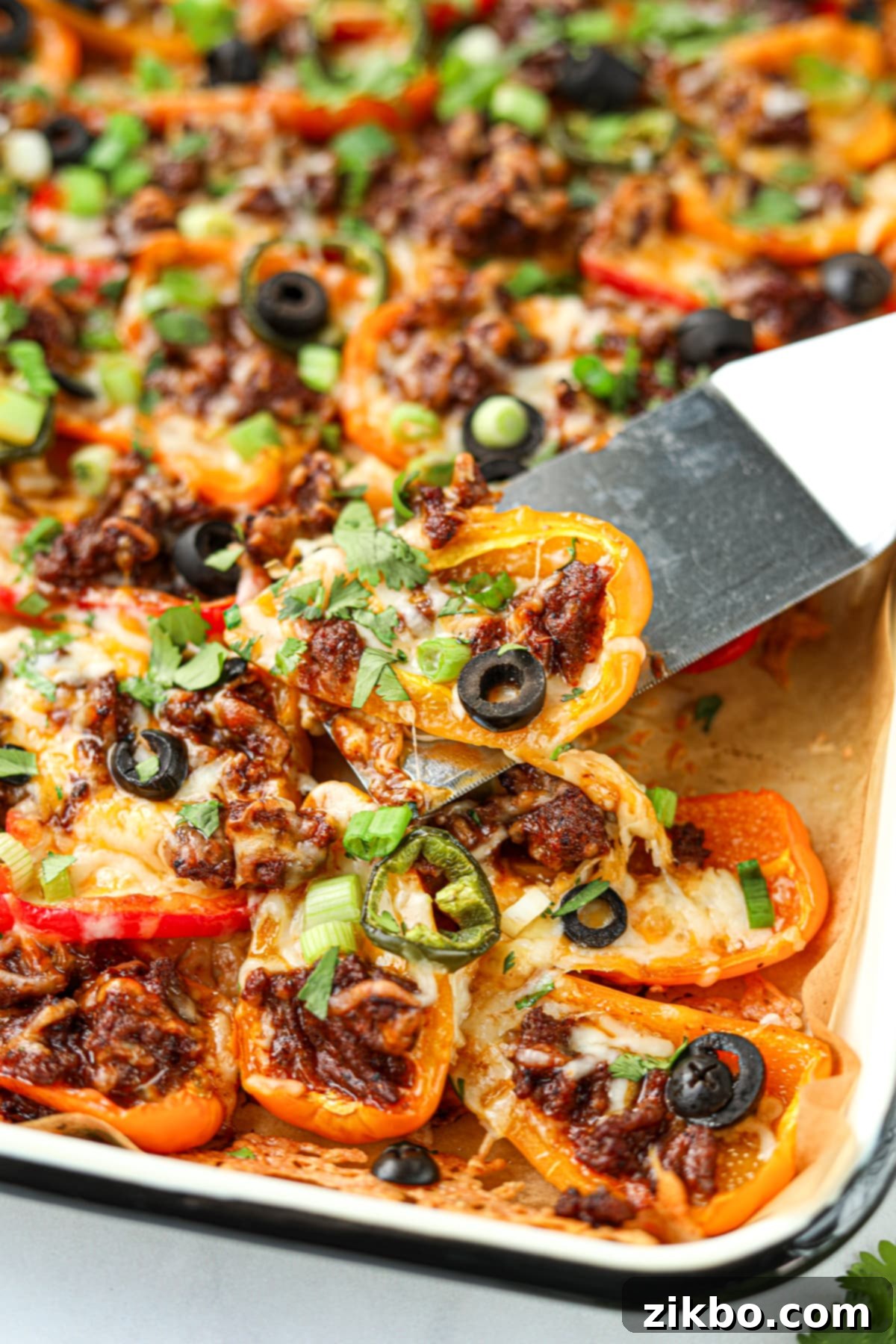 Carefully lifting bell pepper nachos from a sheet pan with a small spatula.