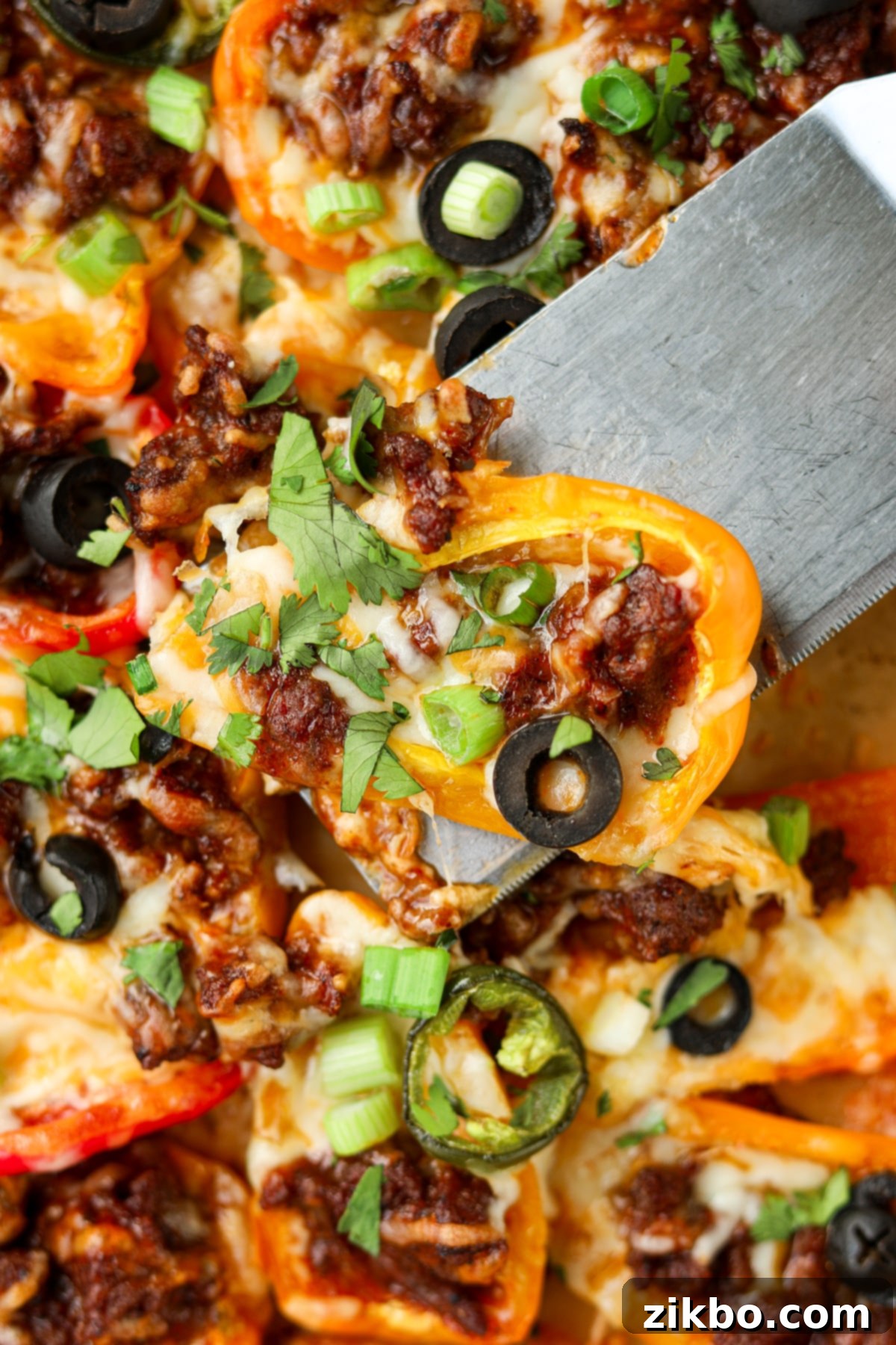 Lifting a mini pepper topped with nacho toppings from a sheet pan.