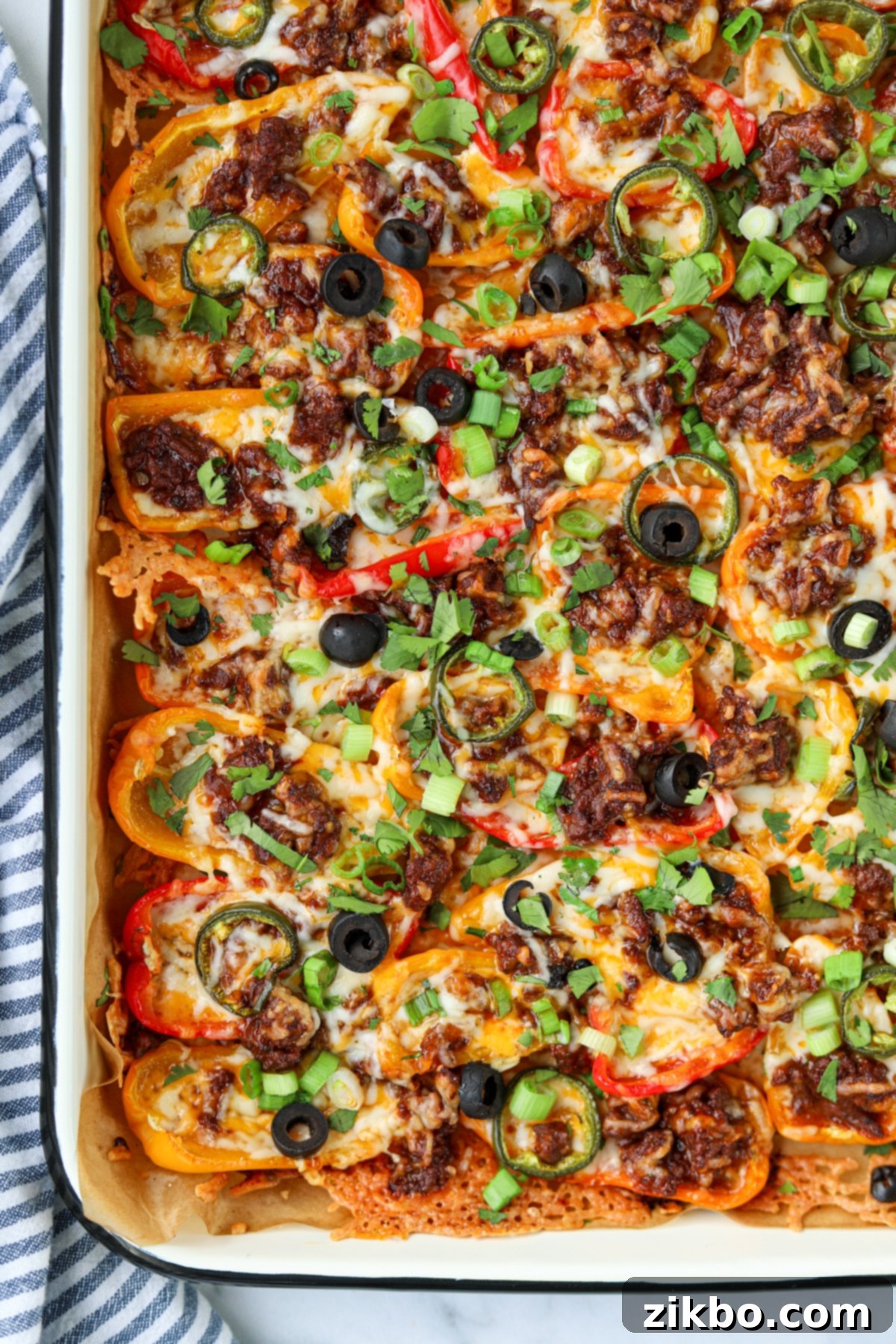 A pan filled with mini pepper nachos, topped with melted cheese, olives, jalapenos, etc.