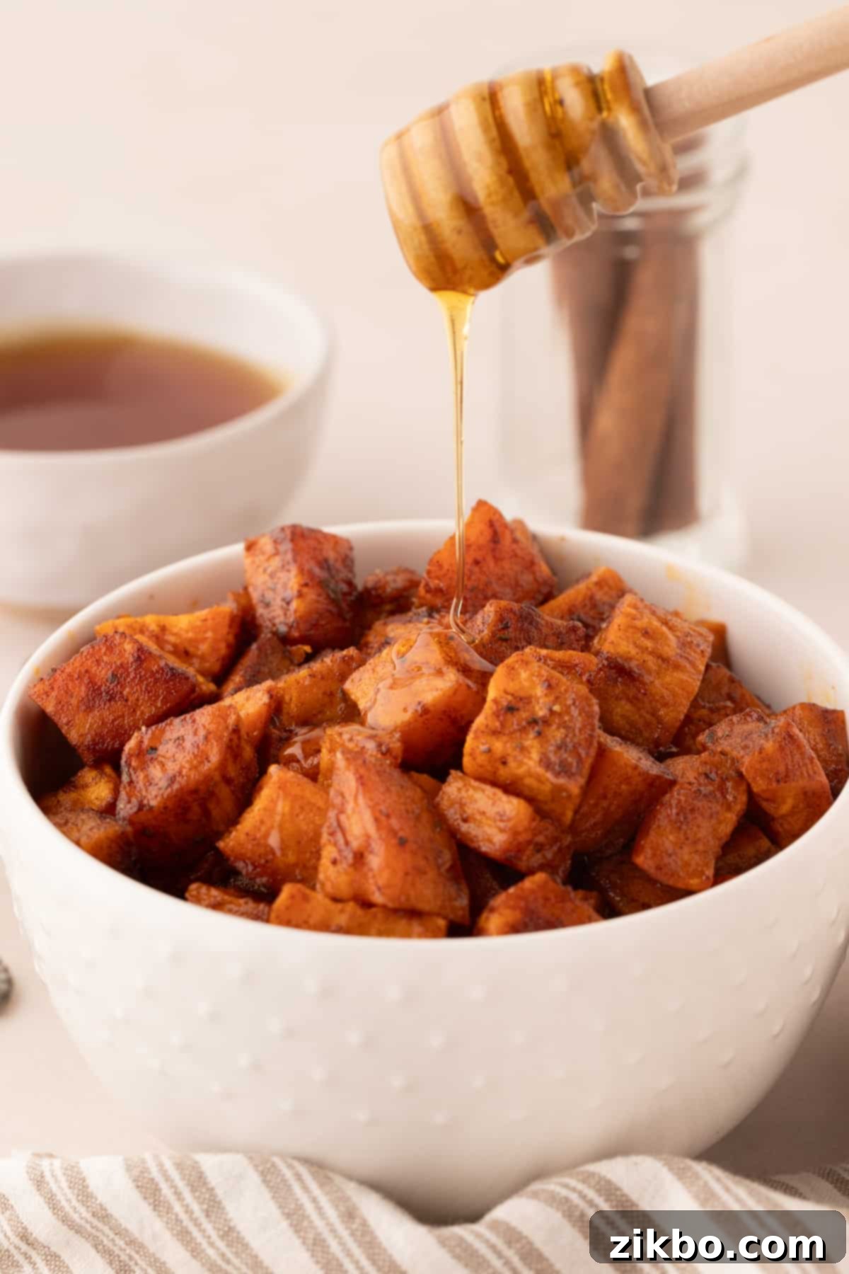 A bowl of roasted sweet potatoes with honey being drizzled on top, creating a glossy finish.