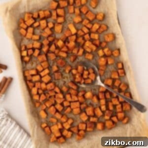 A sheet pan filled with golden-brown roasted sweet potato cubes, with a spoon taking a portion.