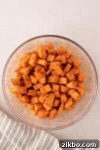 A bowl of cubed sweet potatoes tossed in seasonings and oil.