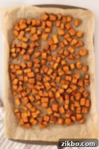 A sheet pan filled with roasted sweet potato cubes that have been seasoned.
