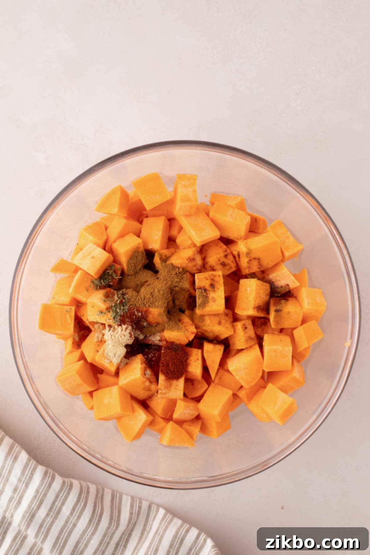 A bowl of cubed sweet potatoes with seasonings sprinkled on top, before tossing.