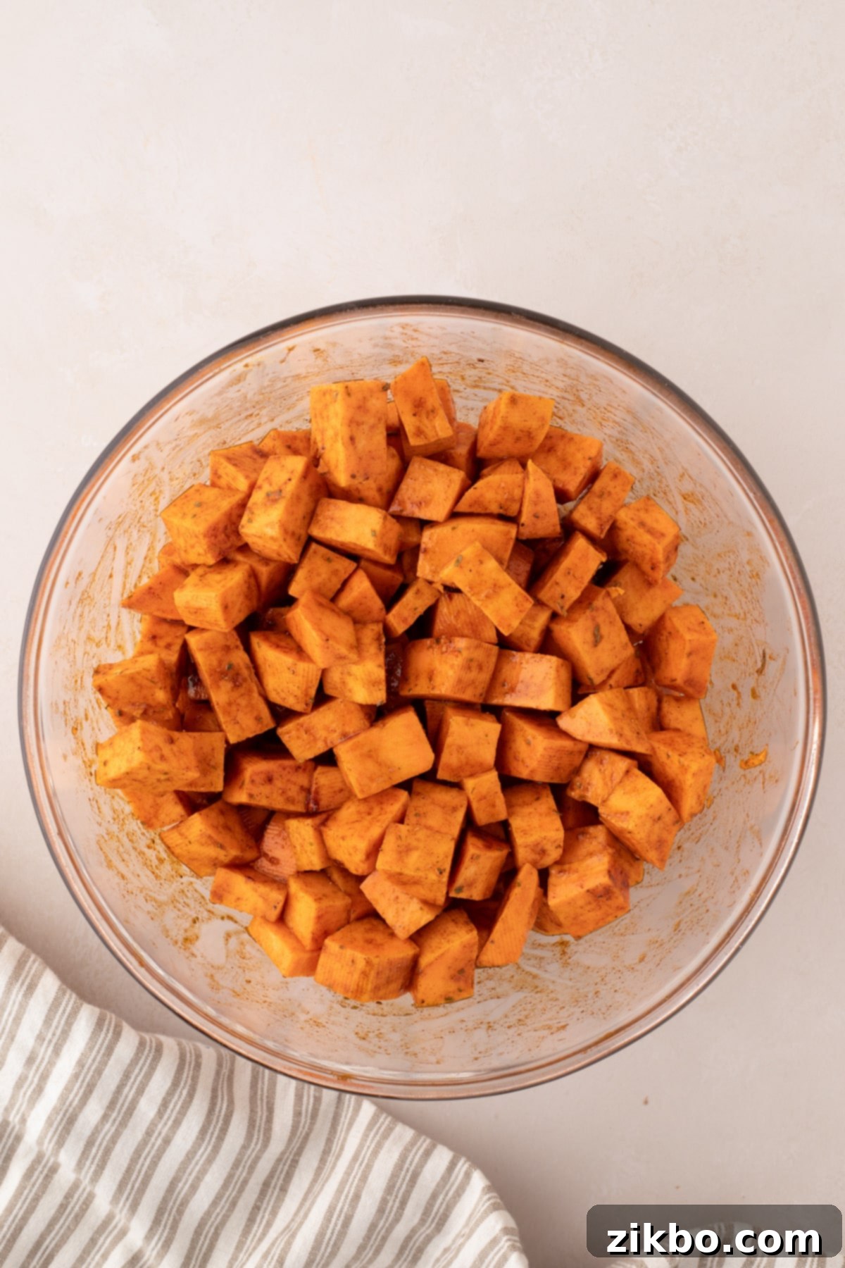A bowl of cubed sweet potatoes perfectly tossed in seasonings and oil, ensuring even coating.