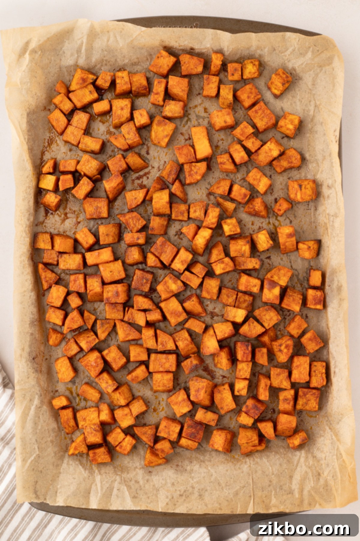 A sheet pan filled with golden-brown roasted sweet potato cubes, showing crispy edges and tender insides.