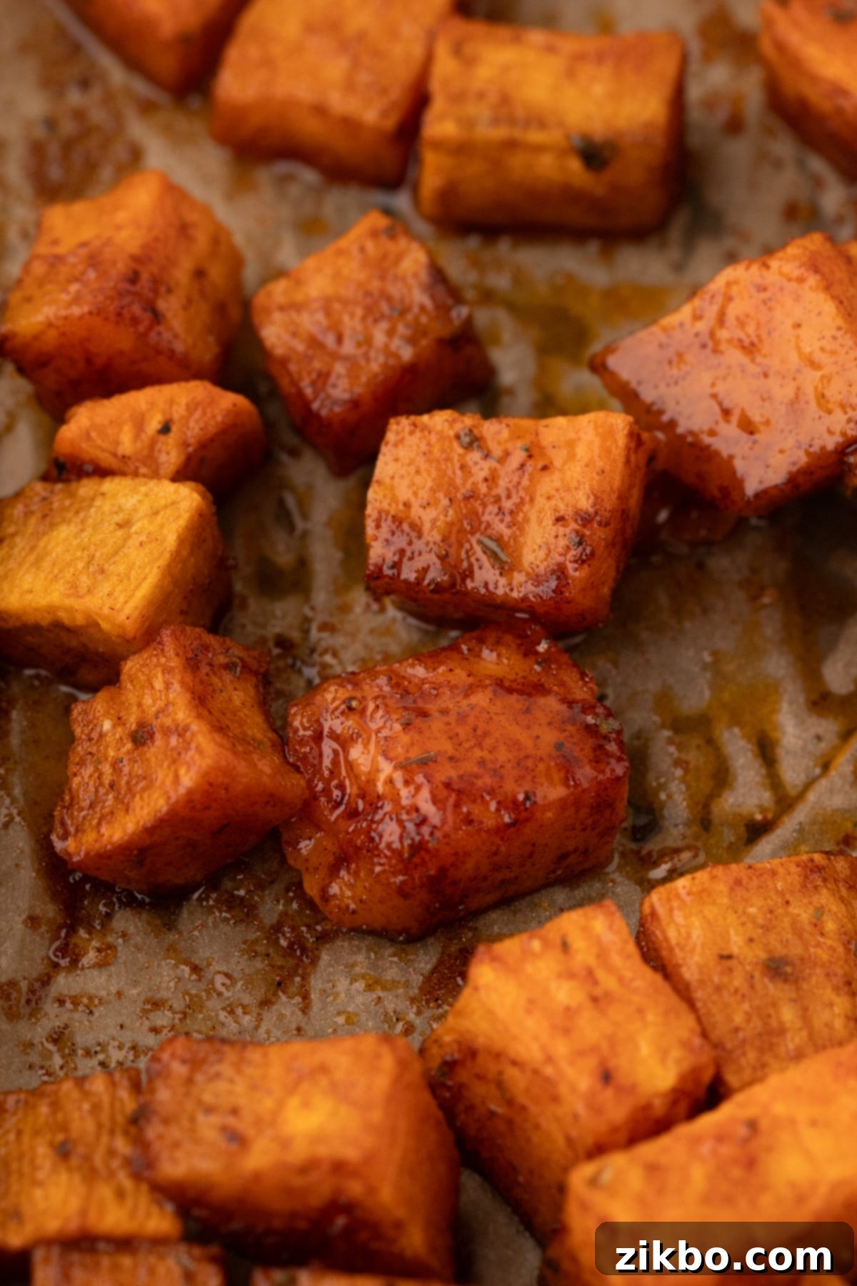 A close up of seasoned sweet potato cubes on a sheet pan, glistening with oil and spices, ready for roasting.