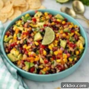 A bowl of cowboy caviar with tortilla chips in the background; topped with a lime wedge, ready to serve.