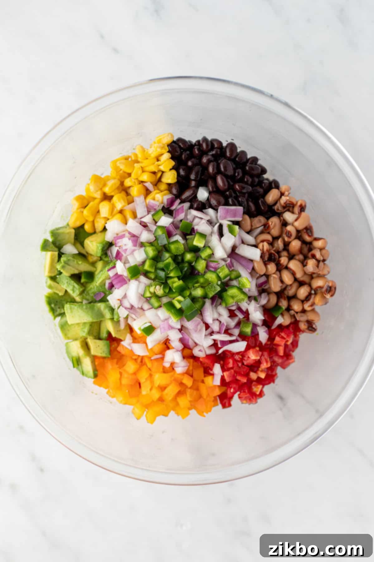 A large bowl filled with a variety of fresh ingredients such as corn, diced bell pepper, cherry tomatoes, and red onion.