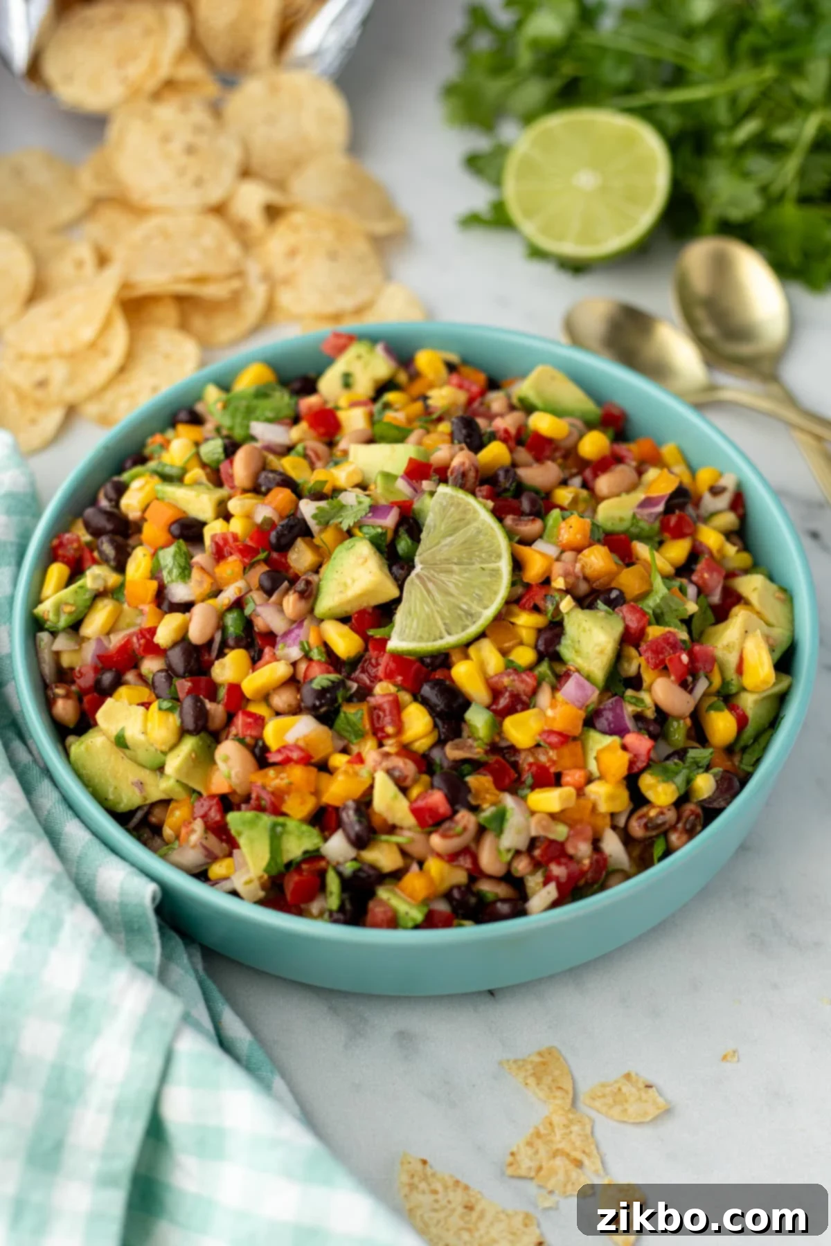 A large bowl filled with cowboy caviar, with a basket of golden tortilla chips blurred in the background.