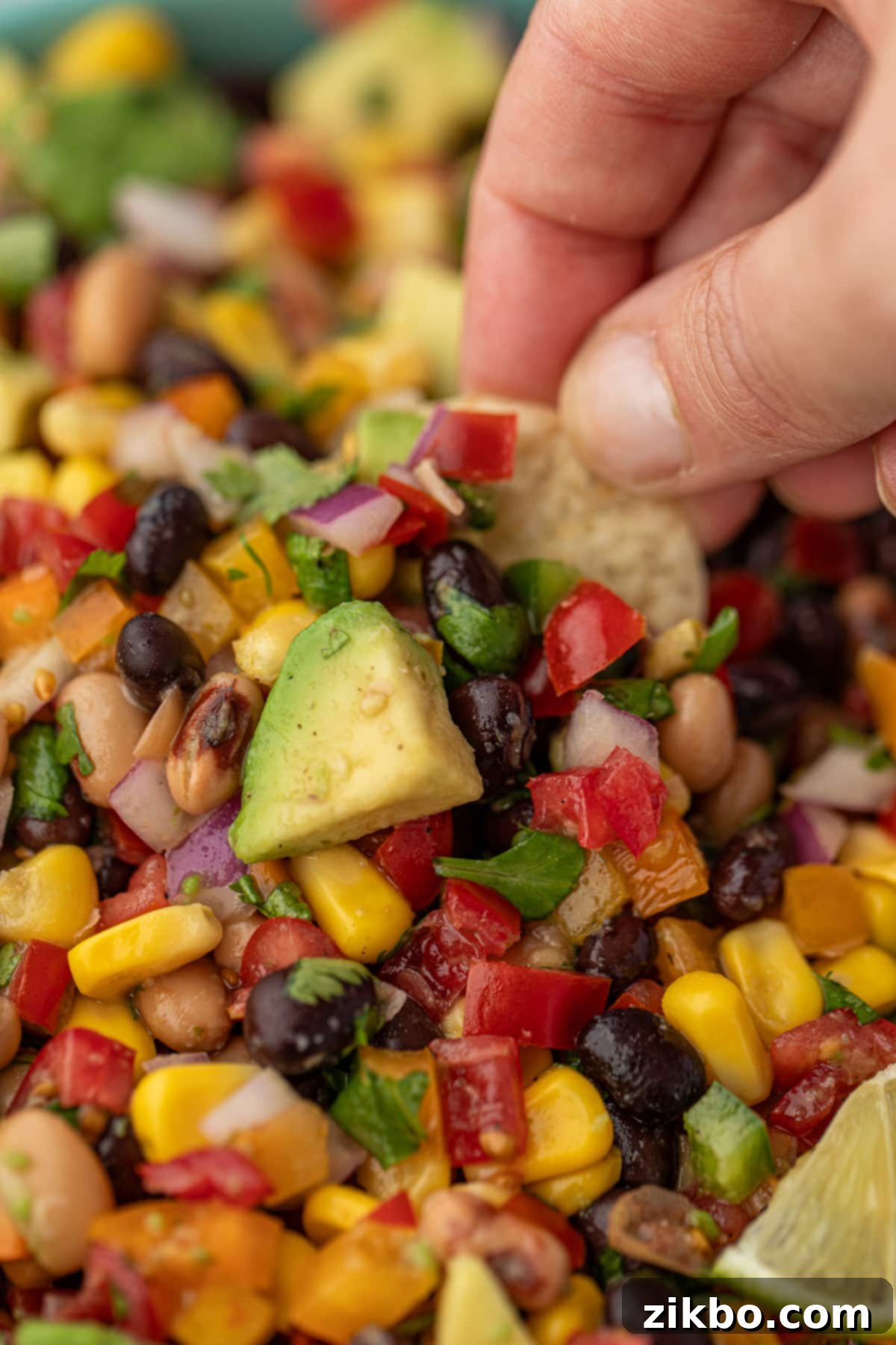 Dipping a tortilla chip into Texas Caviar with corn and avocado visible.
