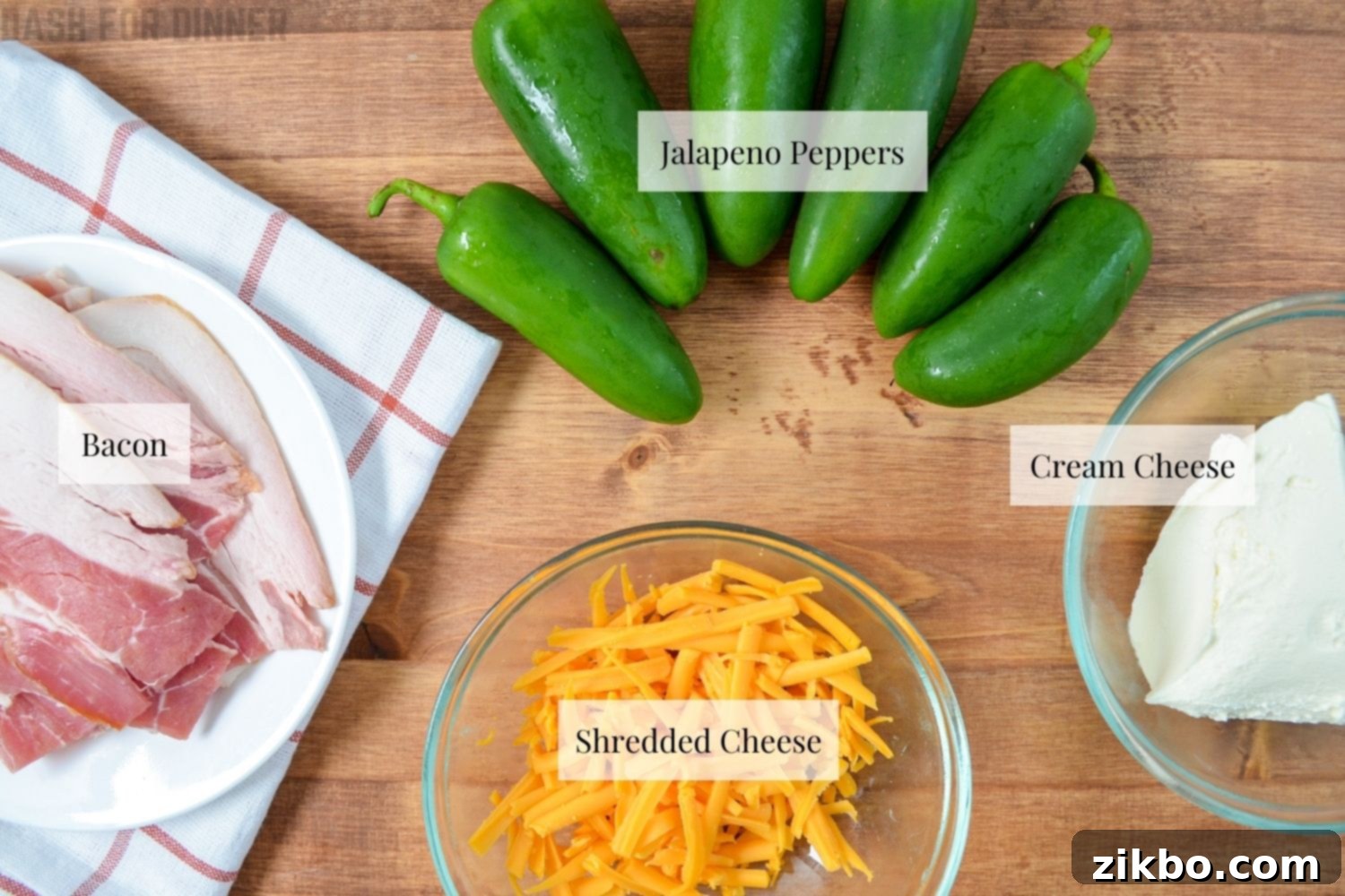 A close-up shot of the simple ingredients needed to make air fryer jalapeno poppers: fresh green jalapenos, a block of cream cheese, a wedge of cheddar cheese, and strips of raw bacon.