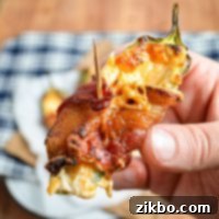 A hand holding up a homemade bacon wrapped jalapeno popper, showcasing its crispy texture and golden-brown bacon.