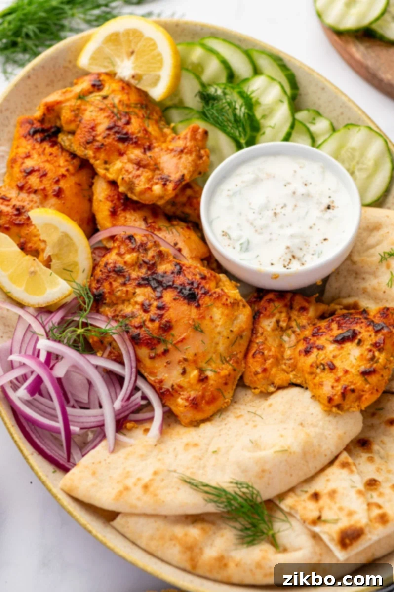 Delicious Greek Yogurt Chicken 11 A platted filled with pita, cucumber, red onion, and seasoned chicken thighs.
