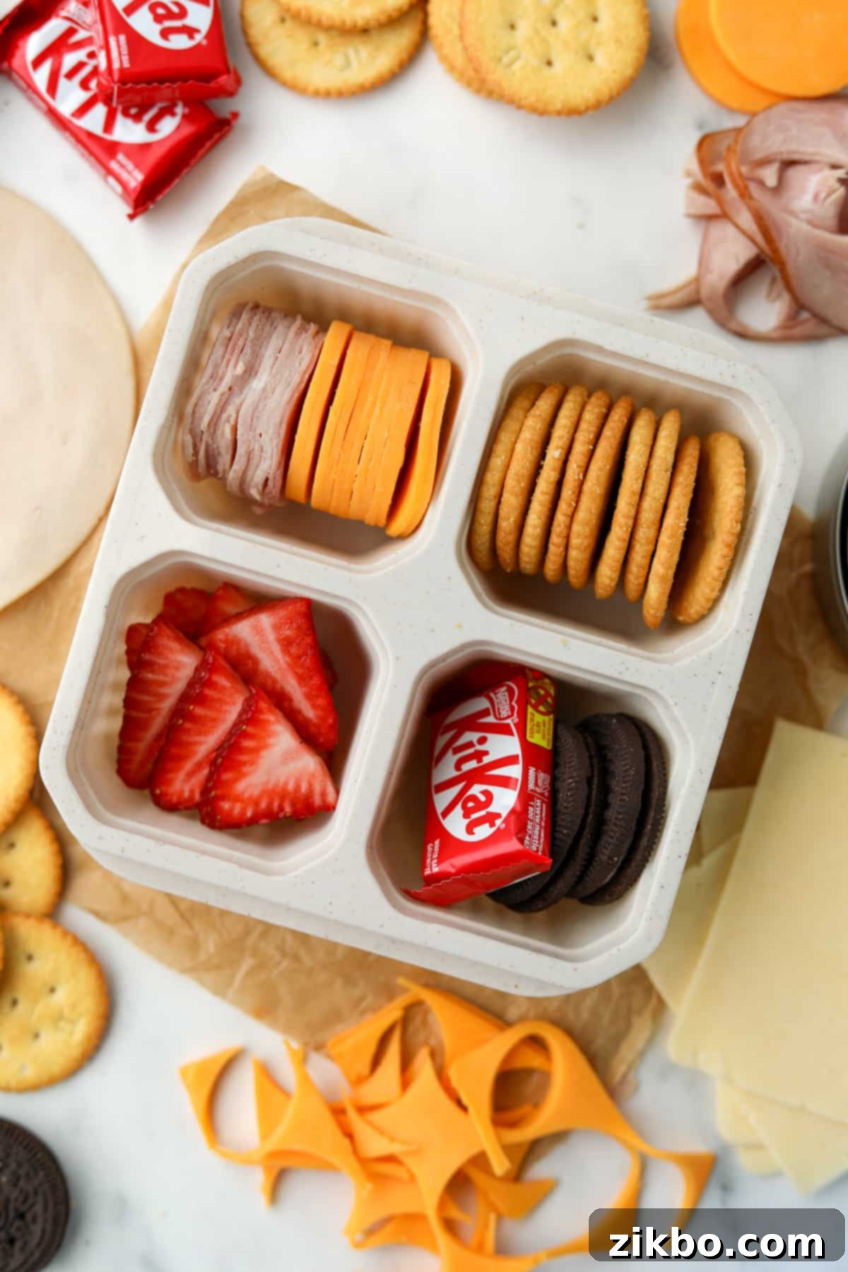 A 4 compartment container showcasing a homemade classic Lunchable with crackers, deli meat, cheese, and sweet treats.