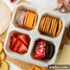 A lunch container with four sections, filled with meat, cheese, crackers, fruit, and a mini chocolate bar, showcasing a homemade lunchable meal.