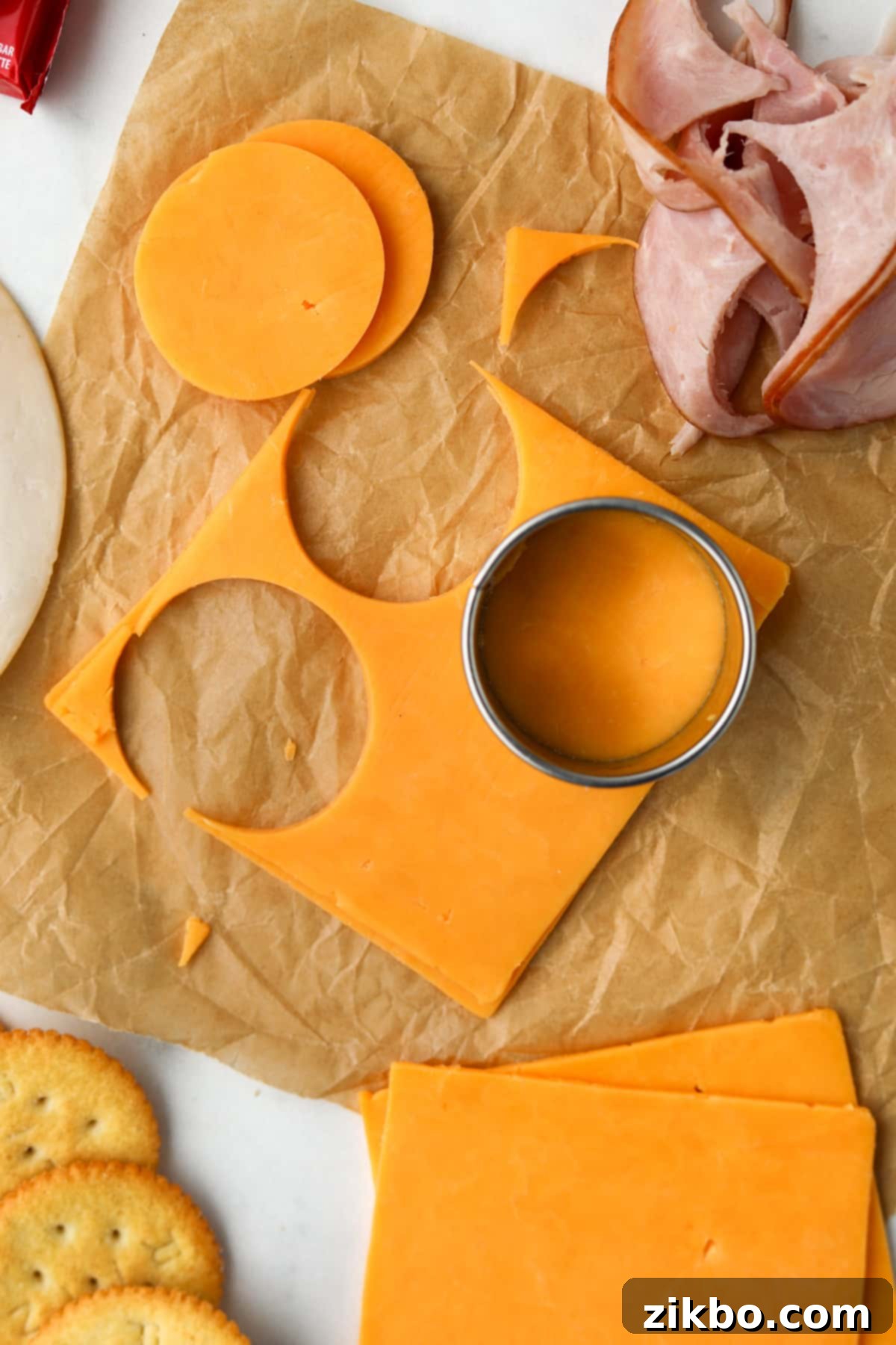 A hand using a circular cutter to slice cheese into rounds, preparing ingredients for homemade lunchables.