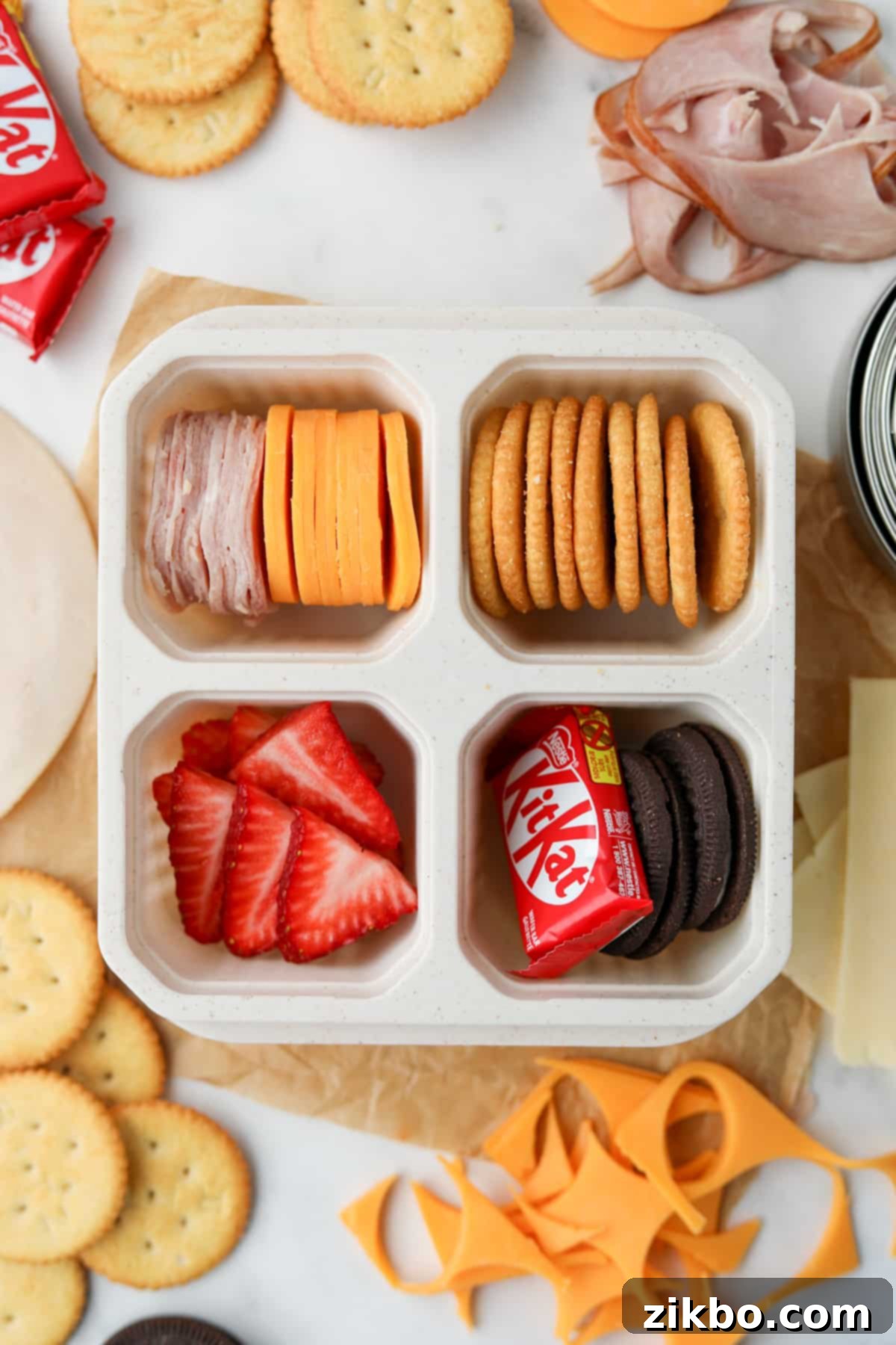 A perfectly packed 4-compartment lunch container filled with cheese, crackers, fresh fruit, and a mini chocolate bar, ready for a grab-and-go meal.