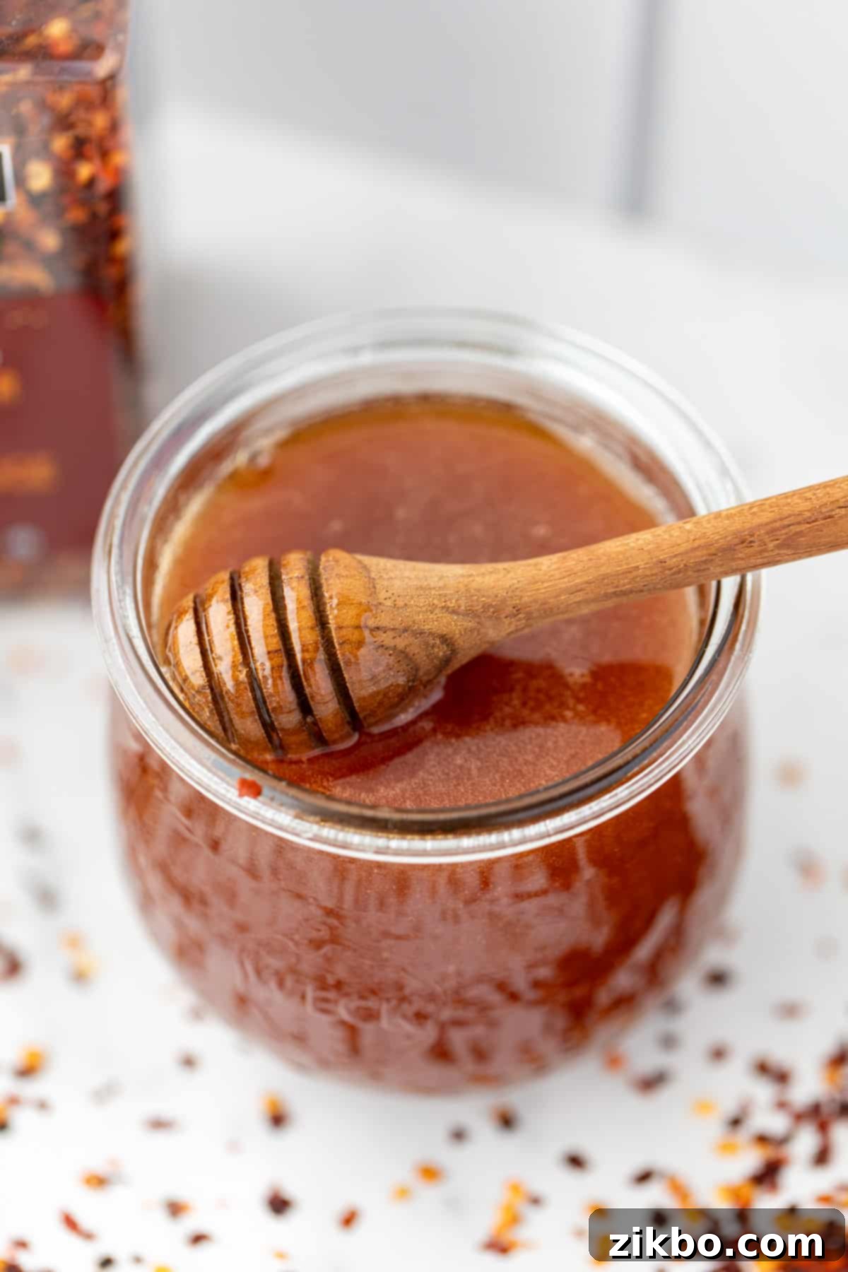 A jar of rich golden hot honey with a wooden honey dipper elegantly resting within, ready to be served.
