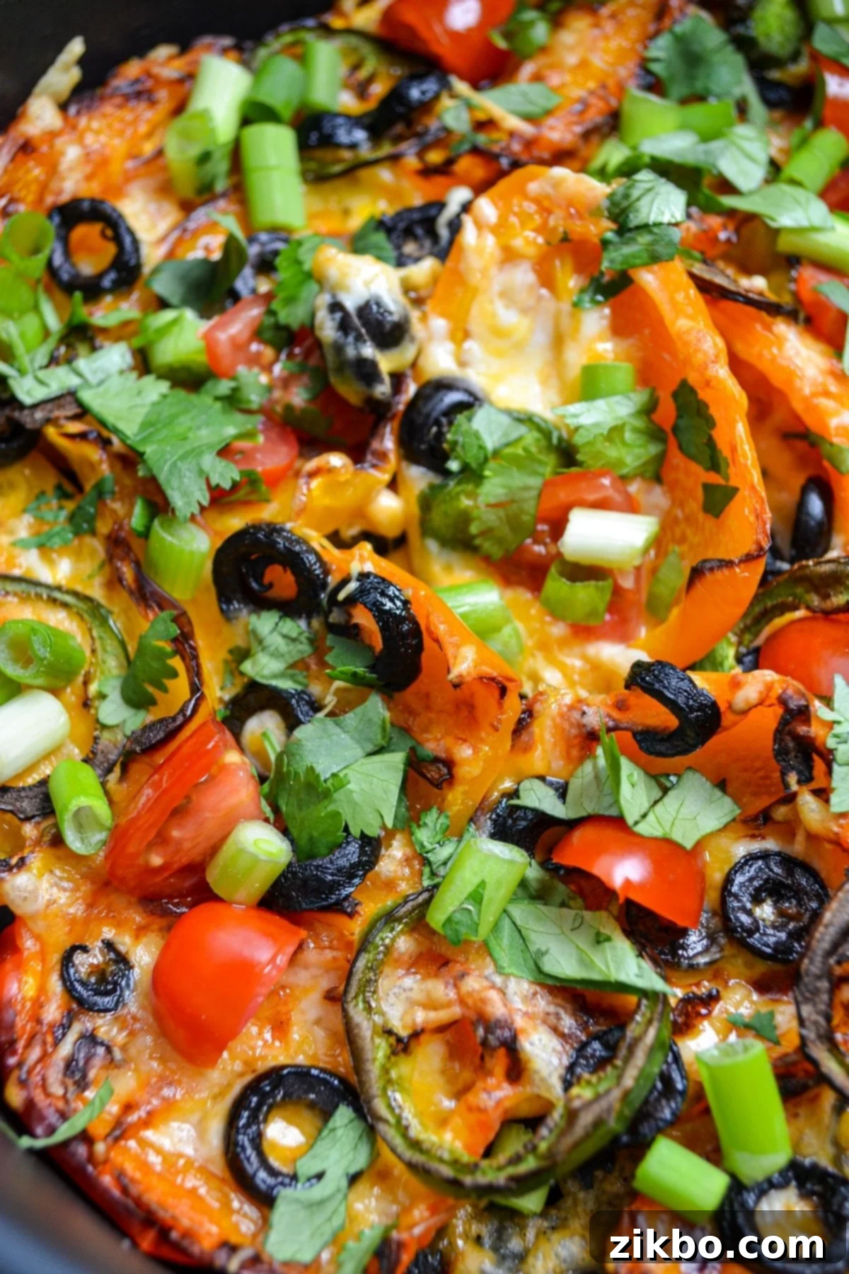 A close up of an air fryer full of mini pepper nachos, showing the melted cheese and toppings.