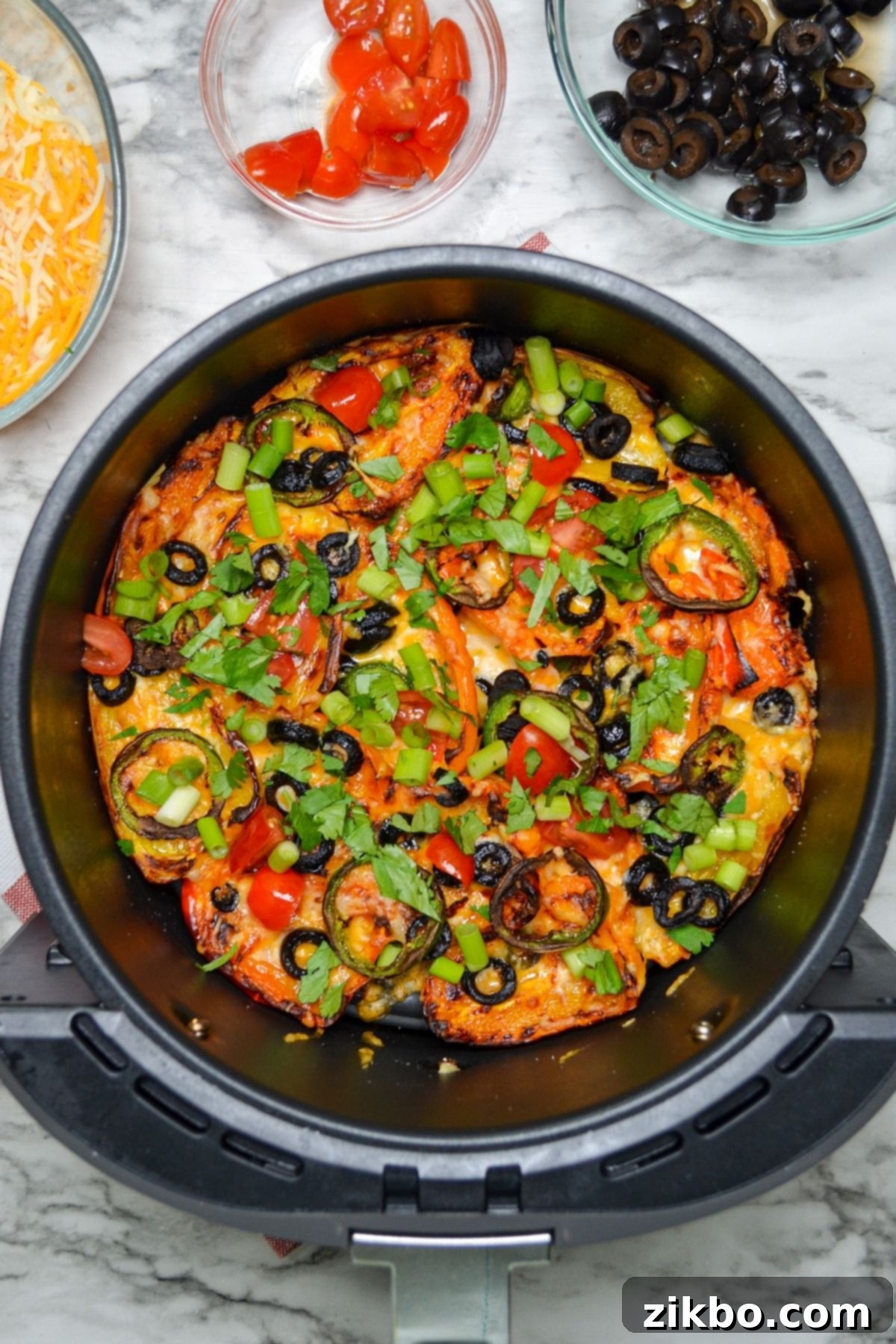 An air fryer basket with mini pepper nachos inside, cheese melted and bubbling.