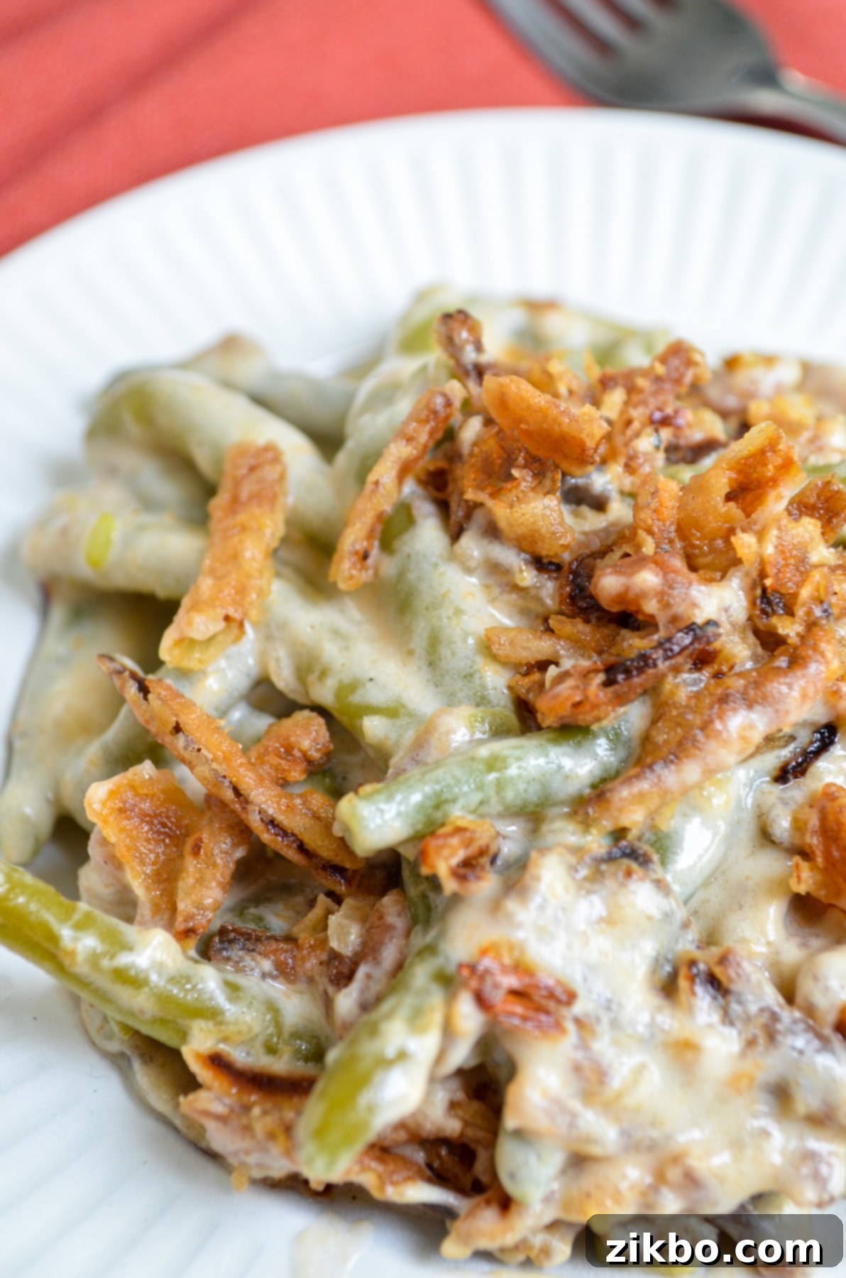 A serving of green bean casserole on a white plate, topped with french fried onions.
