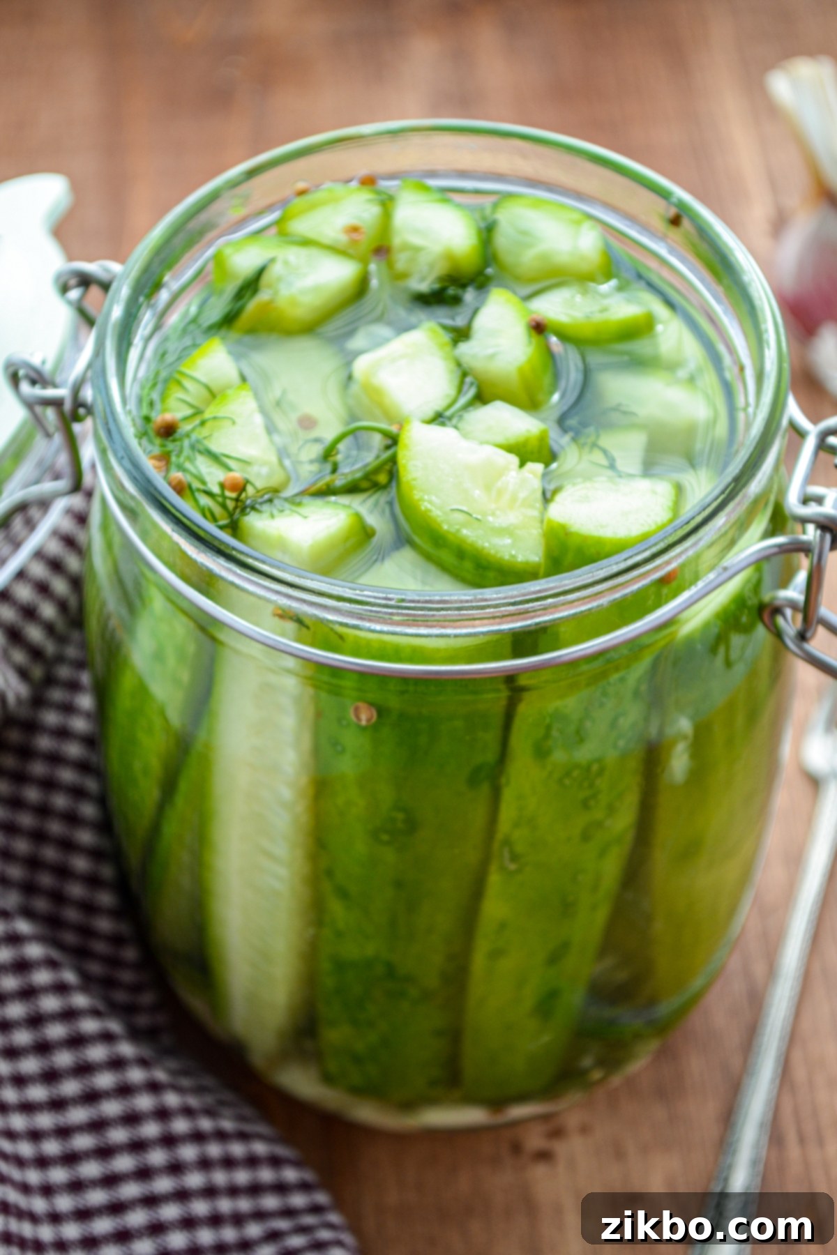 Instant Pot Fast Pickles 3 A jar of refrigerator pickles, resting alongside a gingham napkin, showcasing their vibrant green color.