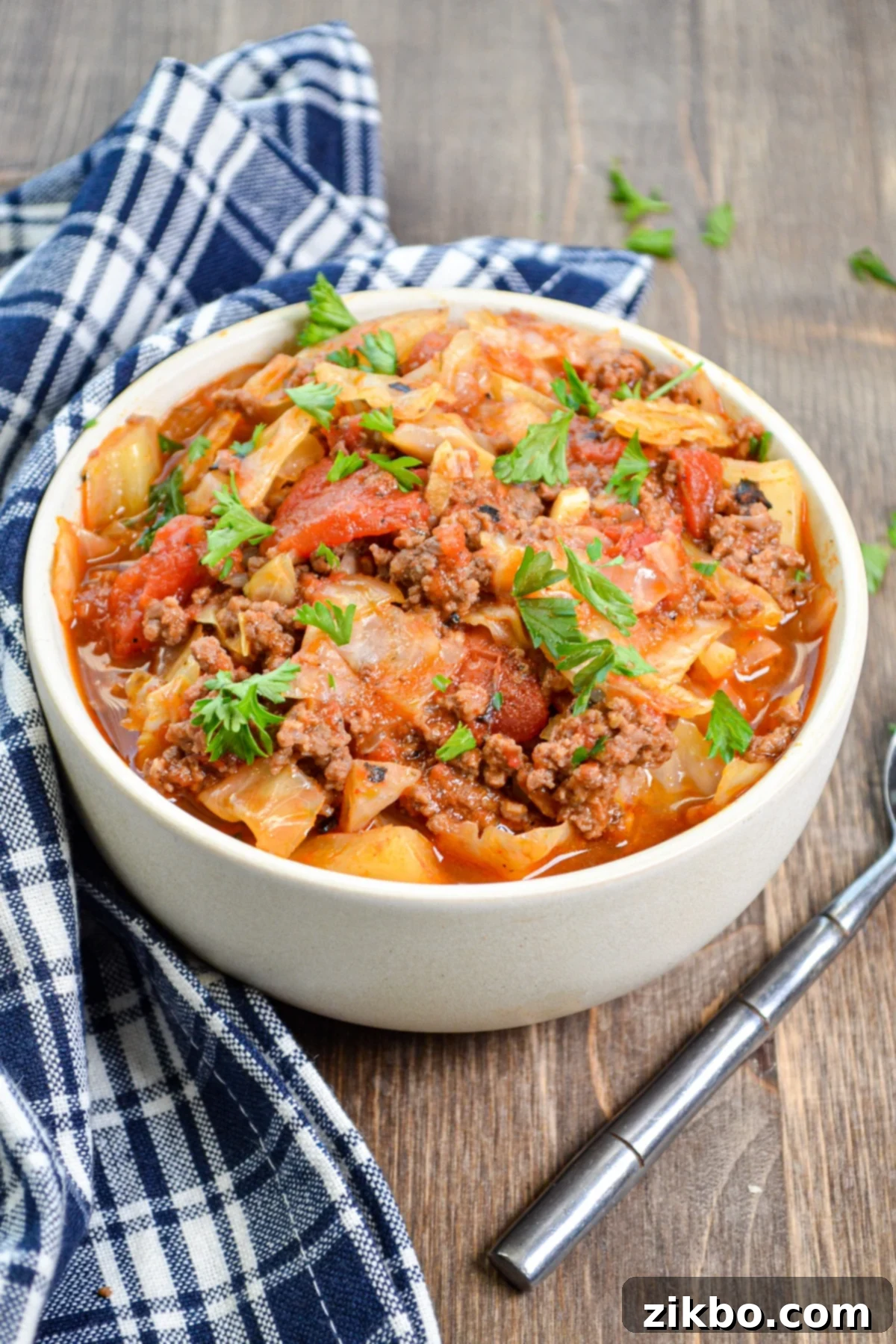 A bowl of cabbage and ground beef hash, filled with tomatoes and topped with parsley.