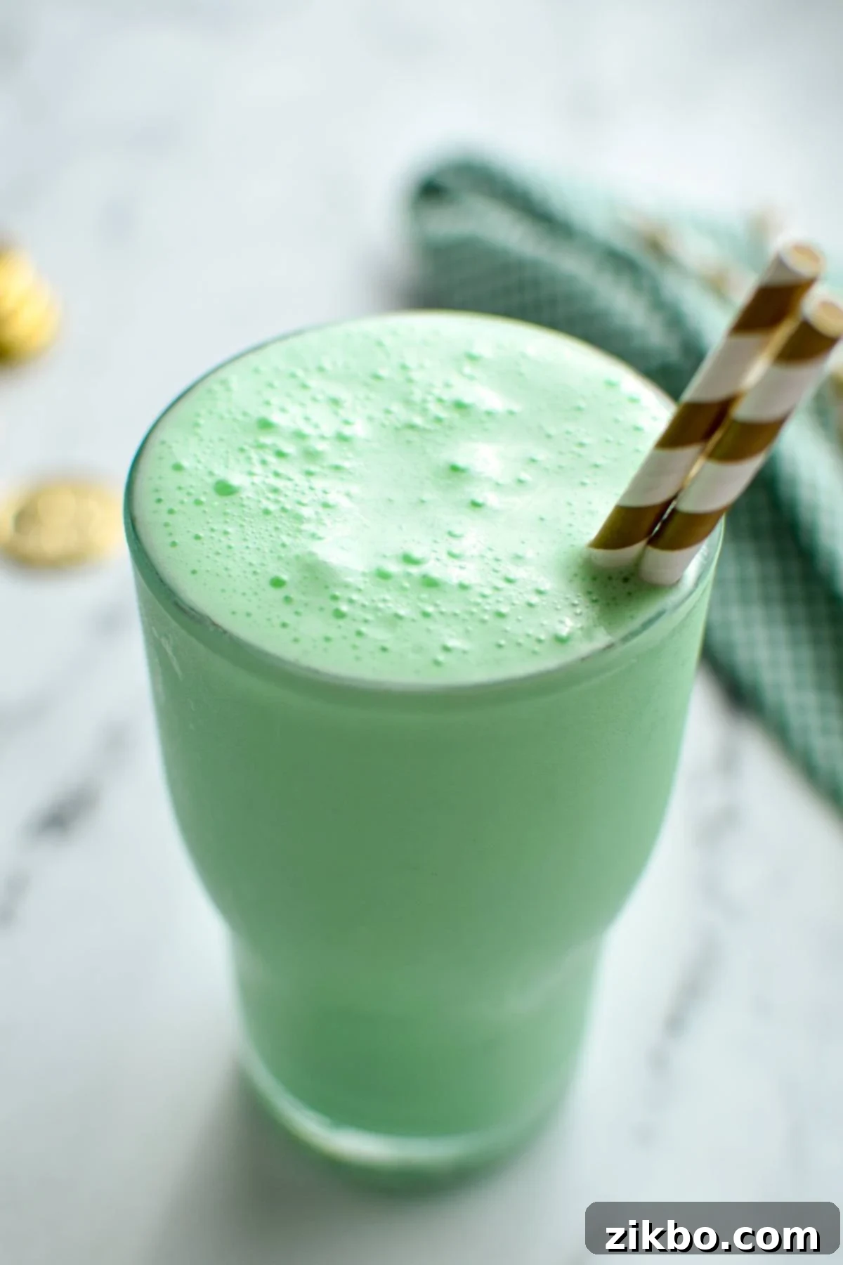 Homemade Shamrock Shake 6 A finished homemade shamrock shake in a clear glass, with a dollop of whipped cream and a gold-striped straw, ready to be enjoyed.