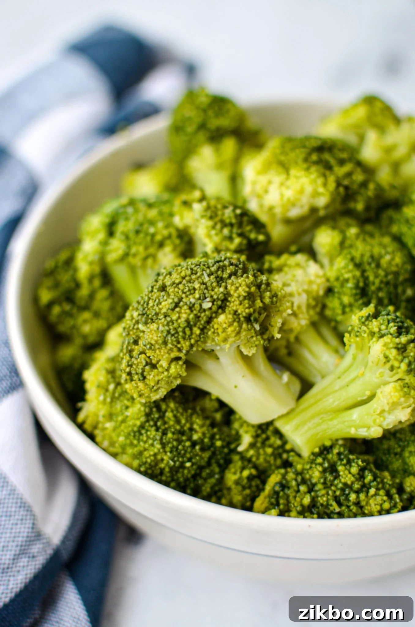 A bowl of cooked broccoli, resting on a blue check napkin.