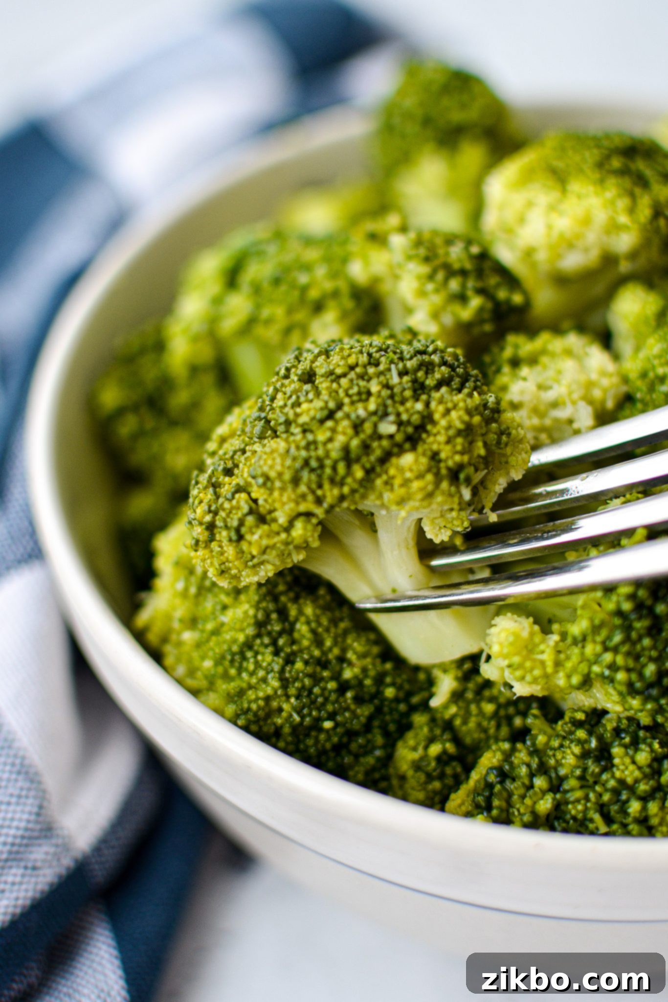 A bowl of cooked broccoli, with a fork taking a piece.